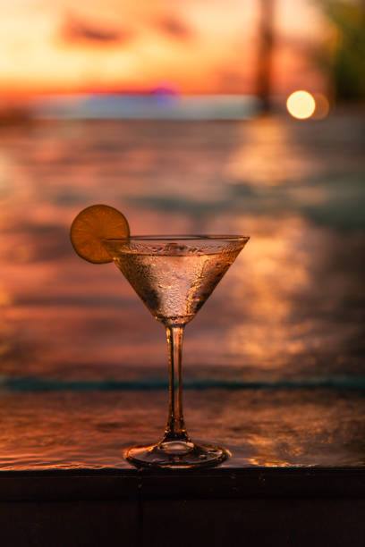 Martini glass cocktail drink standing on swimming pool edge at Maldives luxury hotel during tropical sunset